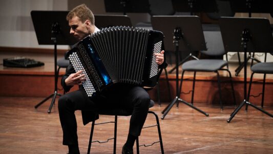 Zdjęcie przedstawia akordeonistę na estradzie podczas koncertu Aco Poznan